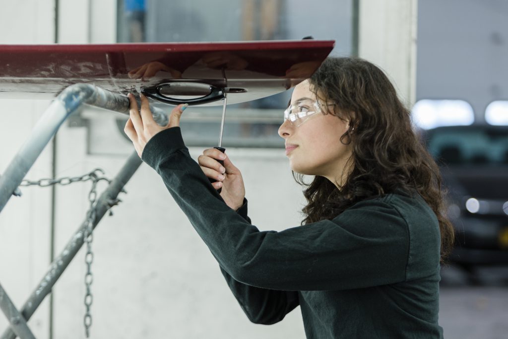 A student wearing goggles works on a car door