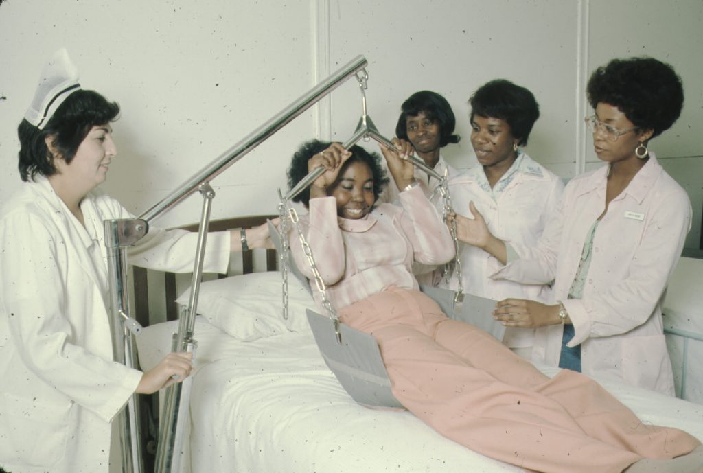 Student nurses practice raising a patient off a bed