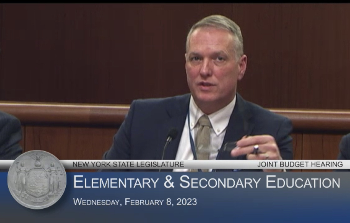 A man speaks above a chyron that reads, "New York State Legislature Joint Hearing, Elementary & Secondary Education, Wednesday, February 8, 2023"