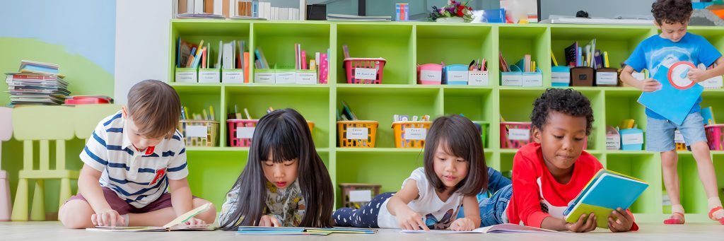 Several children sit and work with colorful shelves behind them