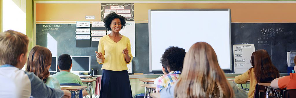 A Black woman stands in a classroom, speaking to seated students