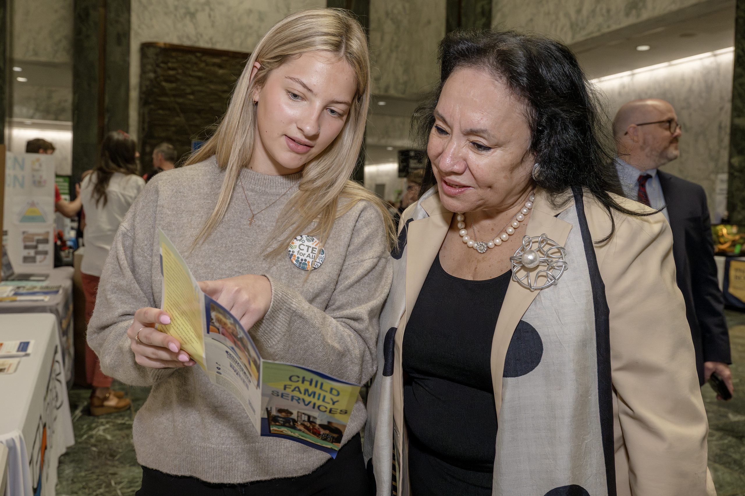 Two women standing next side by side looking at a trifold brochure to discuss its content.