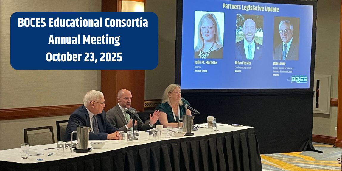 Three people sitting at a table with microphones to speak. Their faces and titles are on a presentation screen off to the side and behind them.