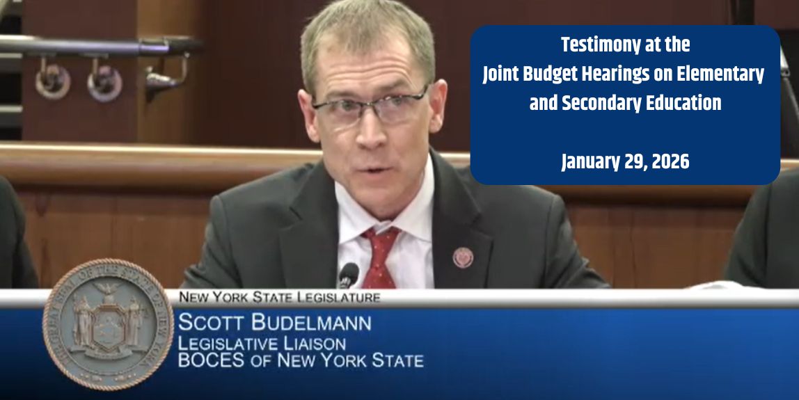 A person is facing forward sitting behind a table to speak.