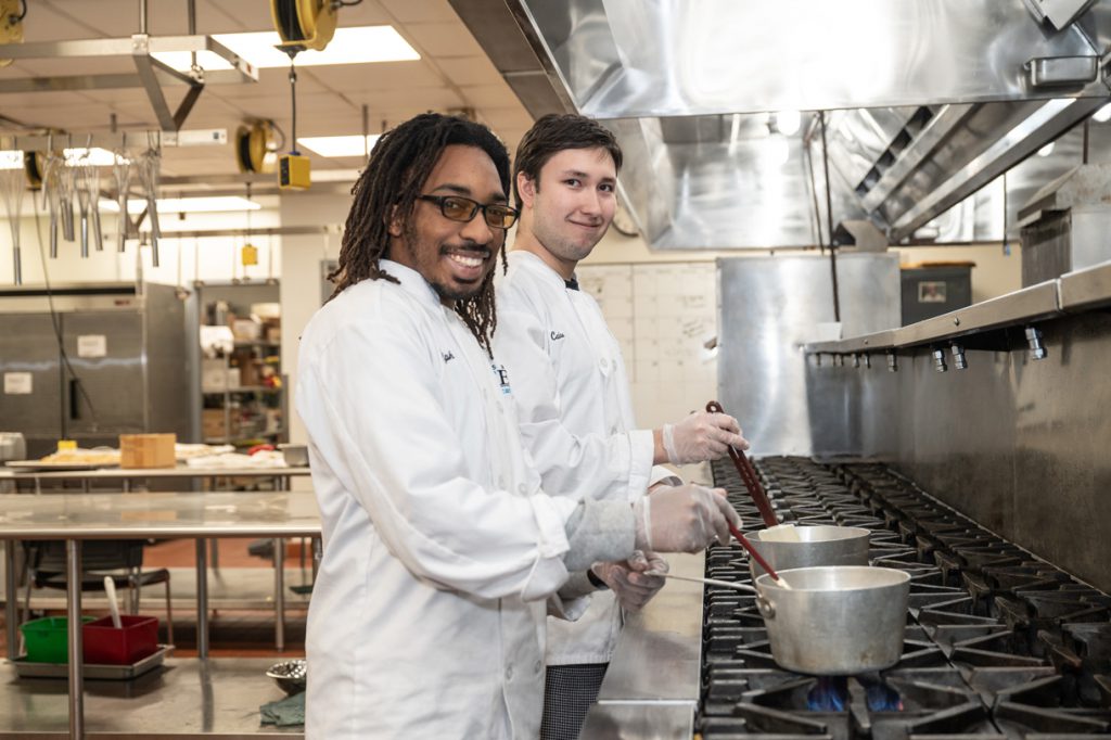 Two male culinary students work at the stove during class.