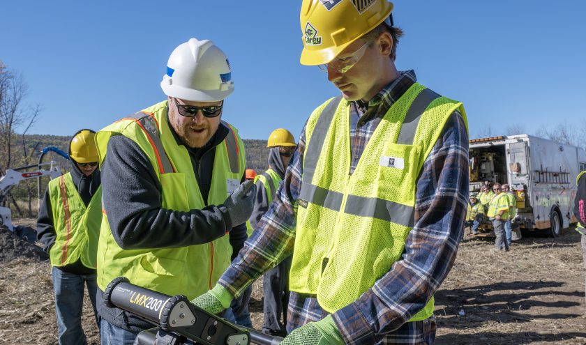 A teacher instructs a construction trades student outdoors.