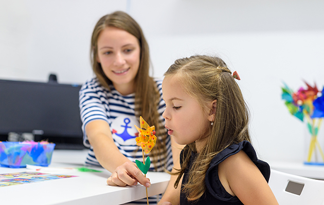 Preschooler blowing into a pinwheel with a teacher.