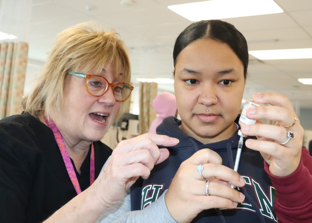 A nursing teacher instructs a student how to fill a syringe.
