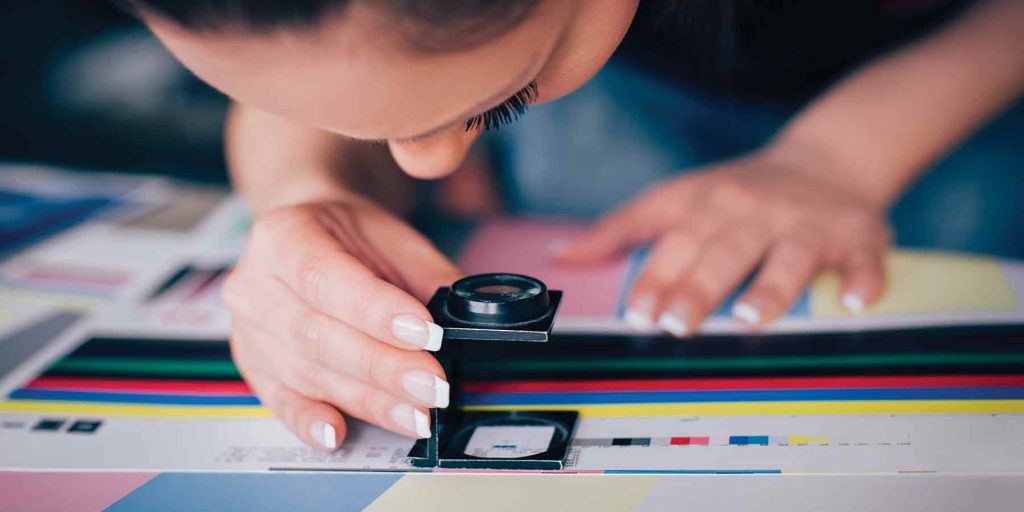 A person looking through a magnifier position over a print sample.