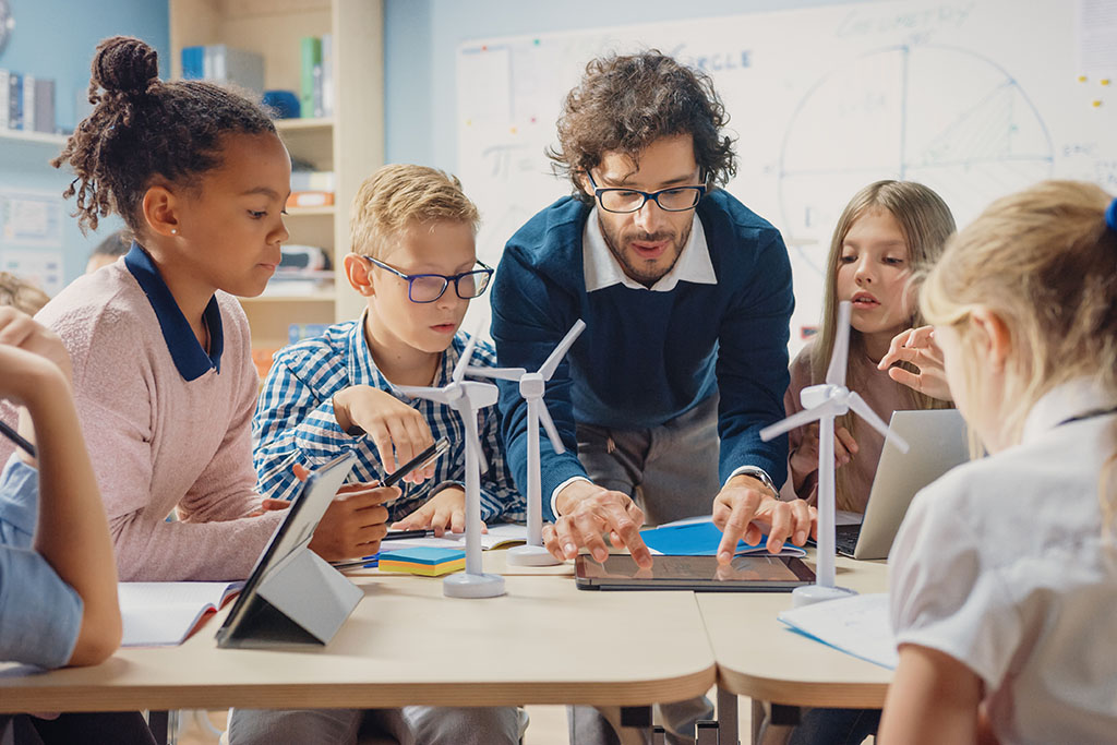 A teacher shows students plans for miniature wind turbines.