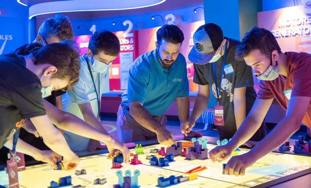 A group of students place figures on a light table while their teacher looks on.