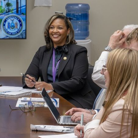 An adult woman smiles while sitting at a conference table with other adults.