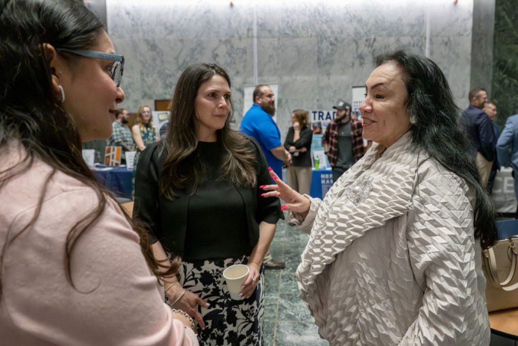 Three women with dark hair in business outfits stand talking to each other