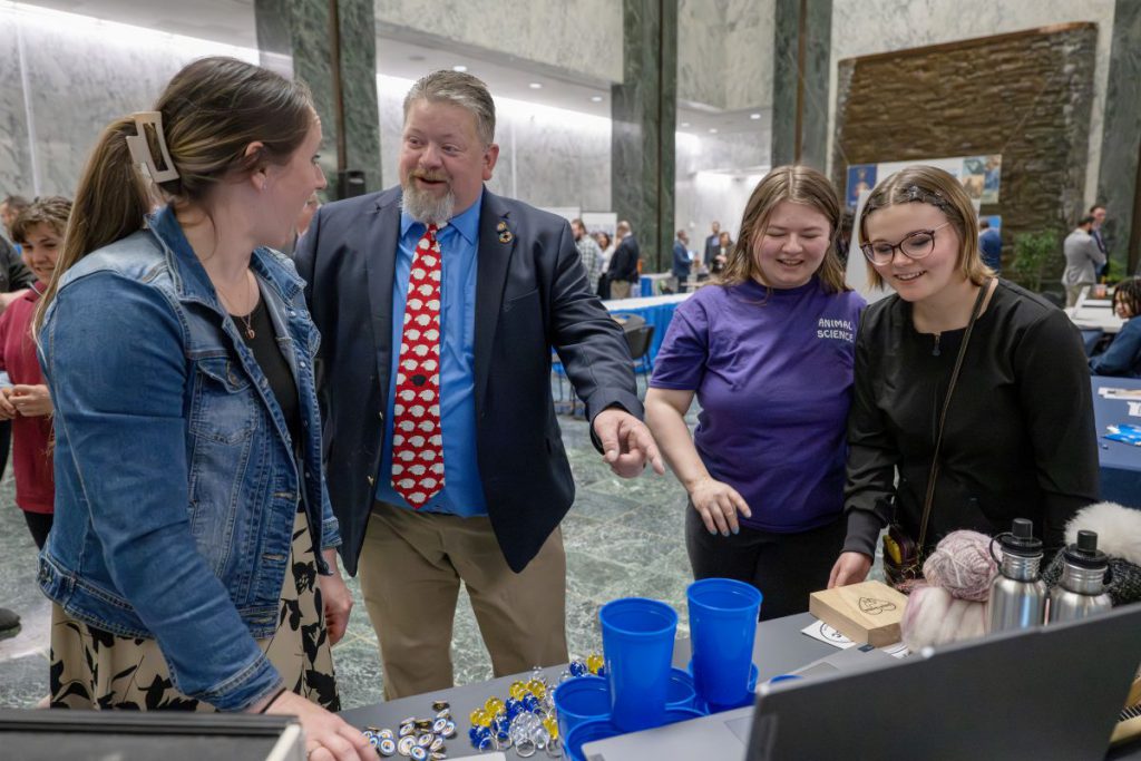 Three females talk with a male legislator at the animal science program table